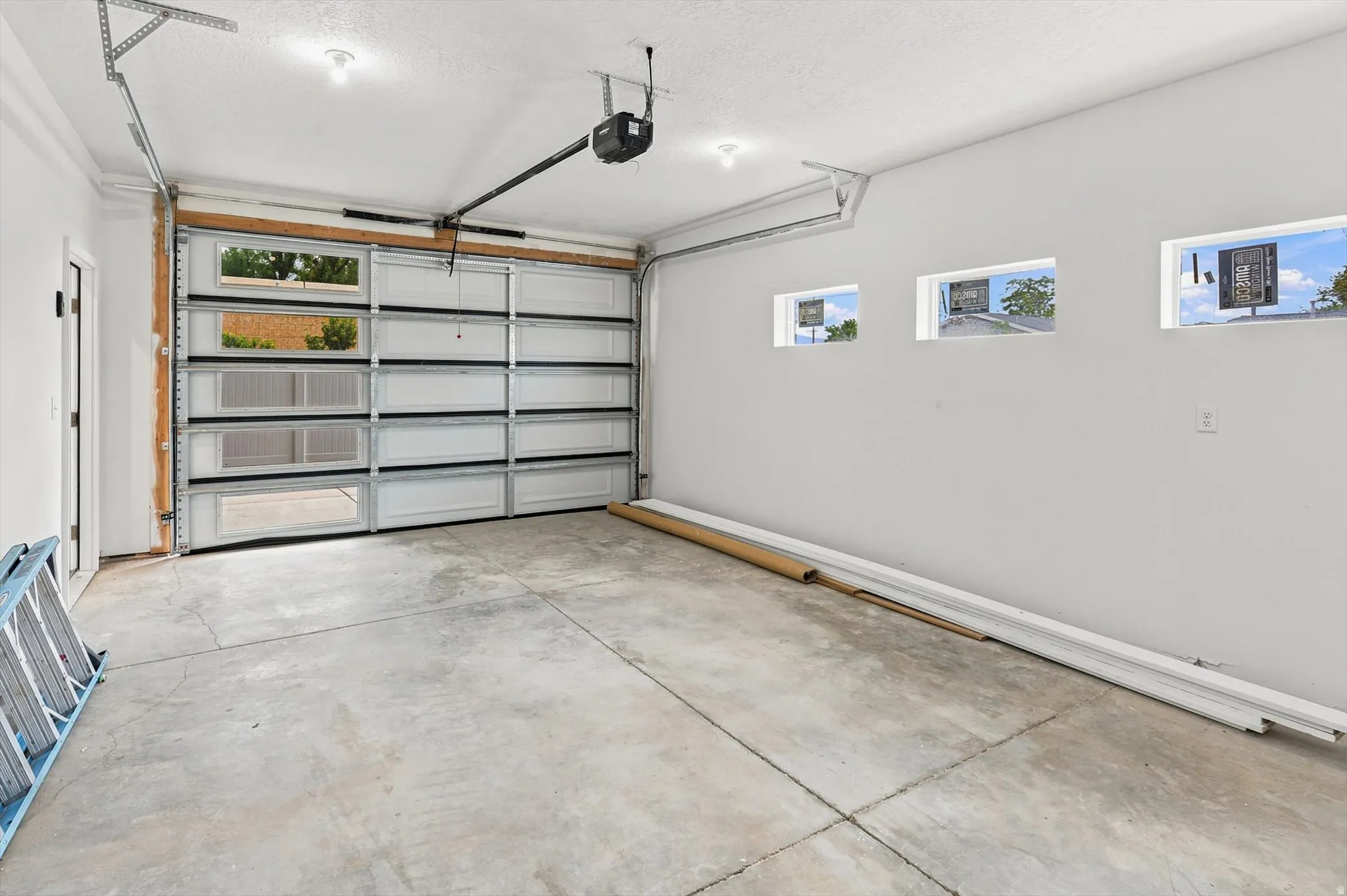 Spacious garage featuring a modern overhead door with clear glass panels, concrete flooring, three high-set windows, and recessed lighting