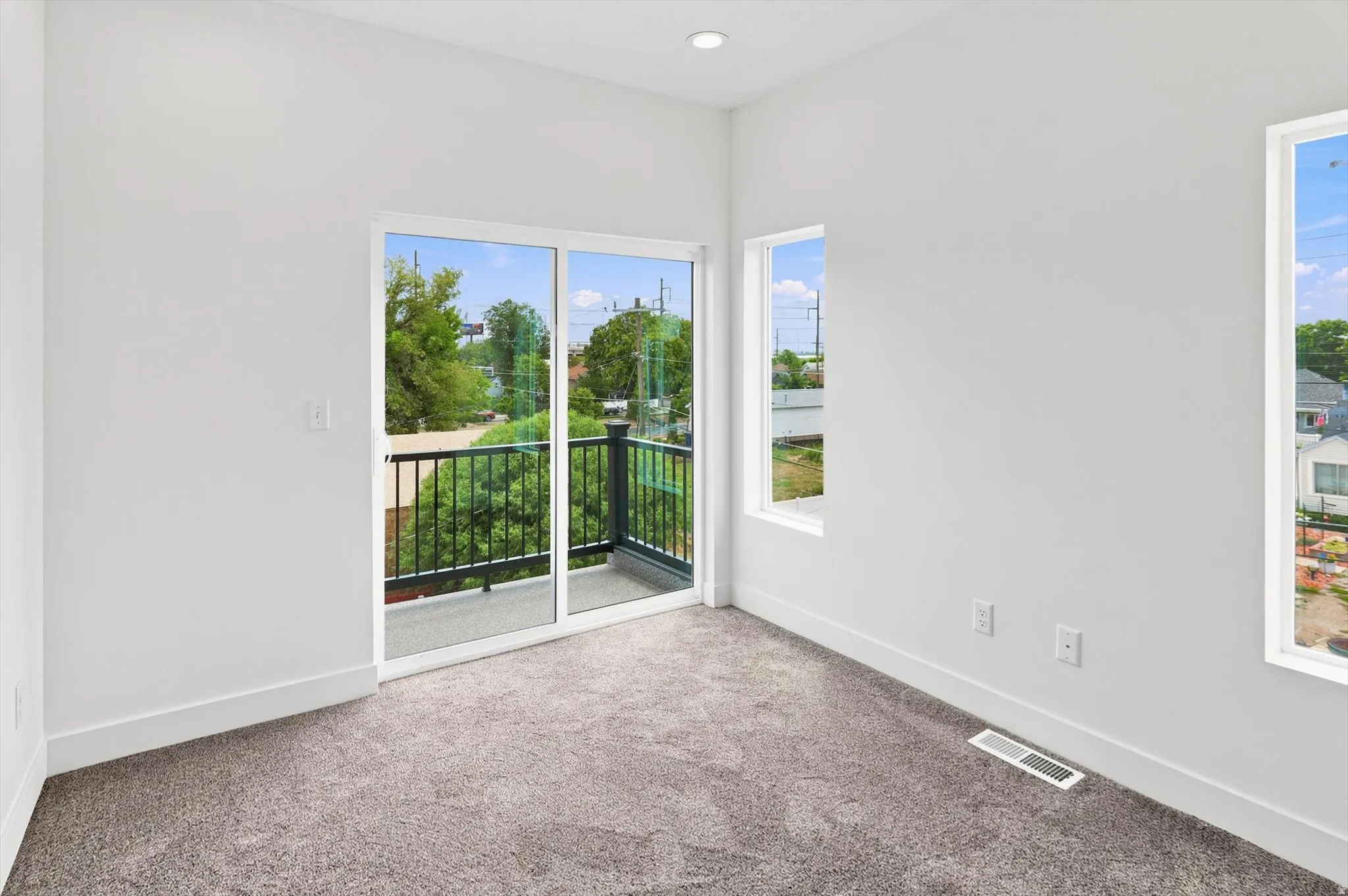 Room featuring a sliding glass door opening to a private balcony with black metal railings, accompanied by two additional windows