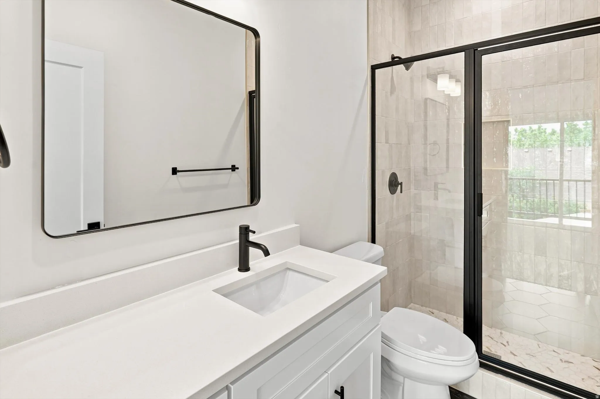 Bathroom featuring a white vanity with integrated sink, matte black fixtures, framed mirror, and a shower with a clear glass enclosure and tile surround