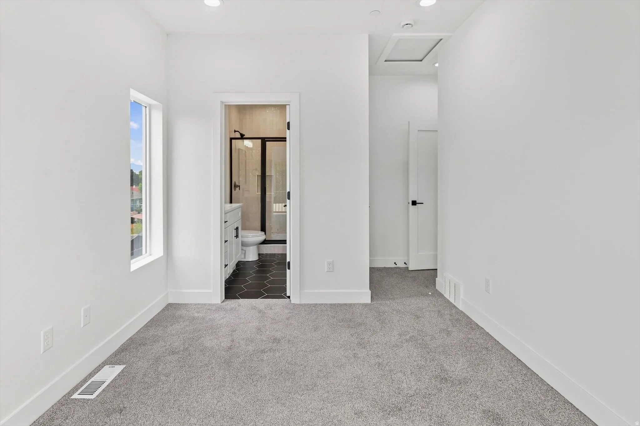 Carpeted room featuring a window with exterior views, recessed lighting, and a bathroom entry with black hexagonal floor tiles