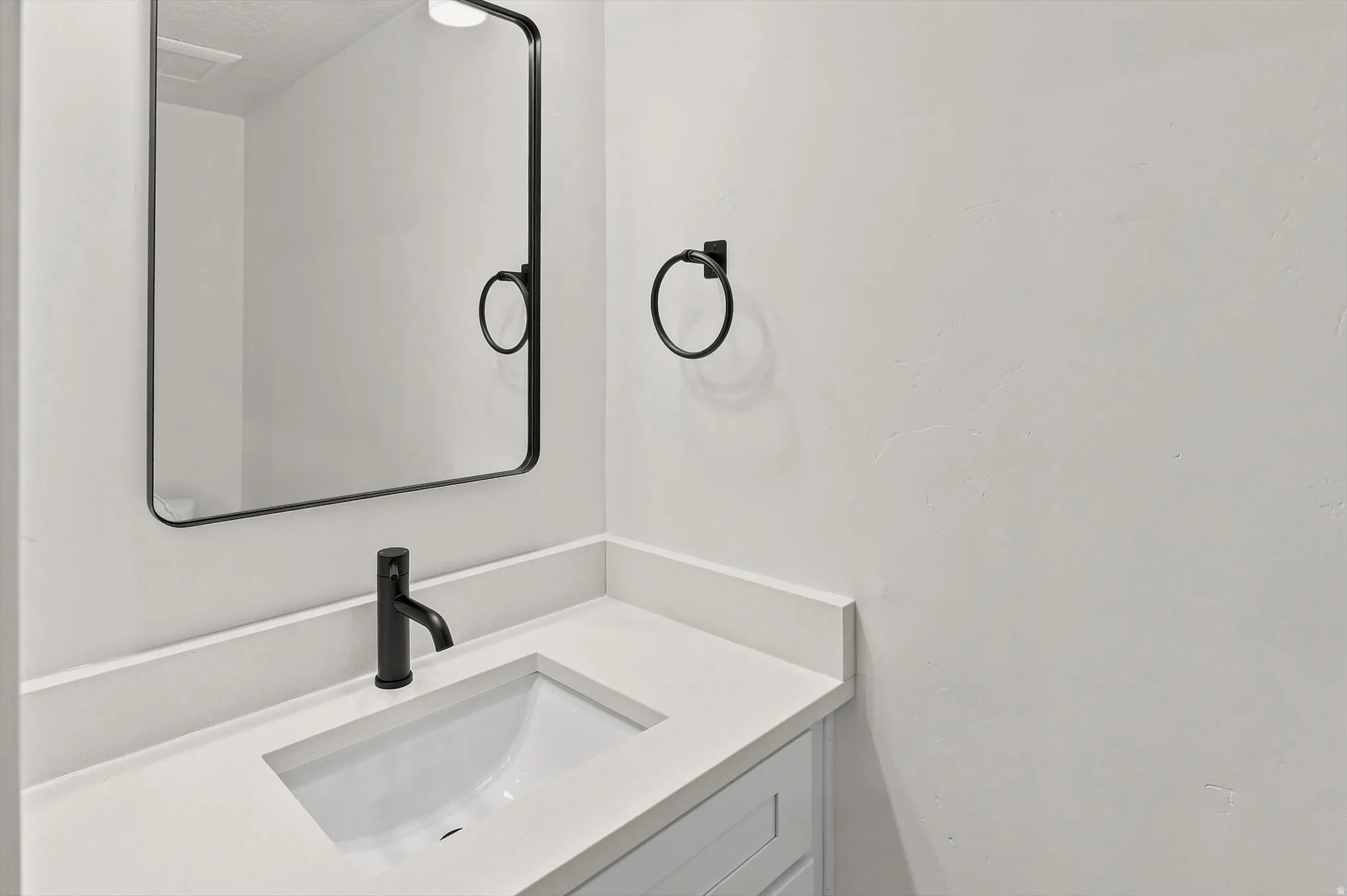 Bathroom vanity featuring a matte black faucet, an integrated sink, and a light-toned countertop