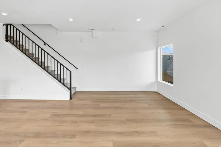 Expansive open living area featuring wood-finish flooring, white walls, and a staircase with a black metal railing