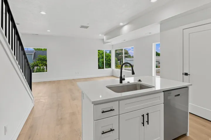 Kitchen island featuring a stainless steel sink, matte black faucet, white shaker cabinetry with black hardware, and an integrated stainless steel dishwasher