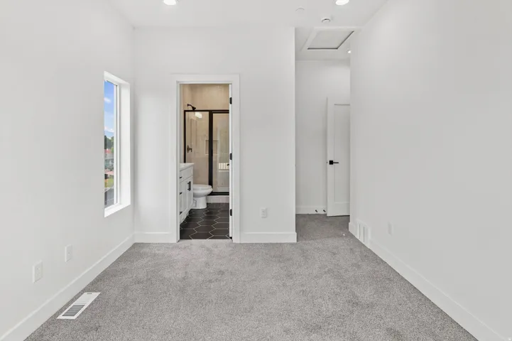 Carpeted room featuring a window with exterior views, recessed lighting, and a bathroom entry with black hexagonal floor tiles