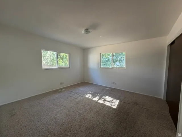 Spacious room featuring neutral carpeting, two windows, and white painted walls