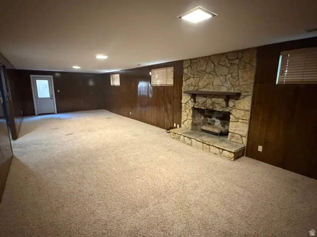 Spacious room featuring a stone-faced fireplace with a wood mantle, paneled walls, and plush carpet flooring