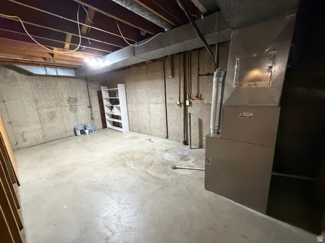 Unfinished basement space with concrete flooring, exposed ceiling joists, and visible utility infrastructure, including a furnace unit