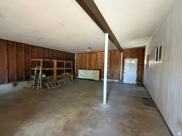 Spacious garage featuring a concrete floor, exposed wood beam, wood plank walls, and a white paneled wall with multiple windows