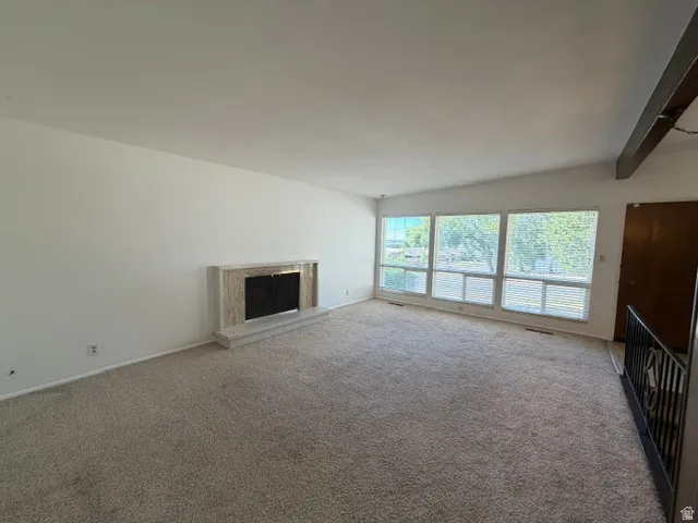 Living area featuring a textured carpet, a fireplace with a stone surround and hearth, and a wall of windows