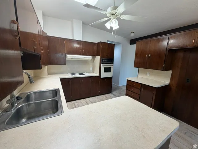 Kitchen featuring extensive wood cabinetry, laminate countertops, a double basin stainless steel sink, built-in wall oven, and an integrated cooktop