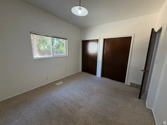 Room featuring vaulted ceilings, carpet flooring, a window offering exterior views, two dark wood-finish bi-fold closet doors, and an overhead light fixture
