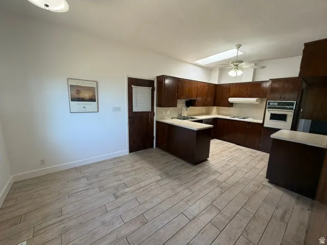 Open-concept kitchen and dining area featuring wood-finish flooring, dark wood cabinetry, a built-in wall oven, and a ceiling fan with integrated lighting
