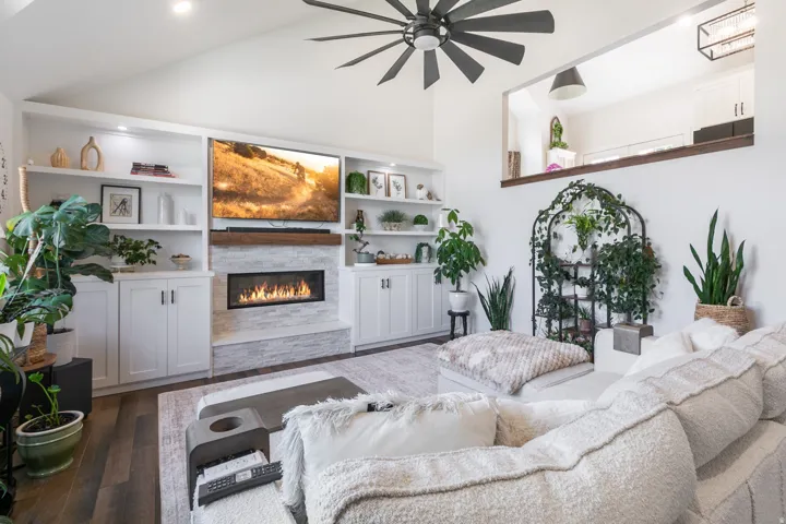 Vaulted living room featuring a linear fireplace with stone surround, custom built-in cabinetry, and wood-finish flooring