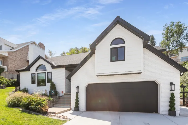 White brick exterior with black trim, a prominent two-car garage, arched window features, and manicured landscaping