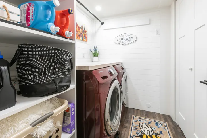 Laundry area featuring wood-finish flooring, white shiplap walls, built-in shelving, and a light-toned countertop