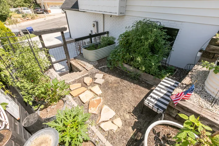 Terraced garden area featuring a stone paver path, raised planter beds, a galvanized steel planter, and exterior access stairs