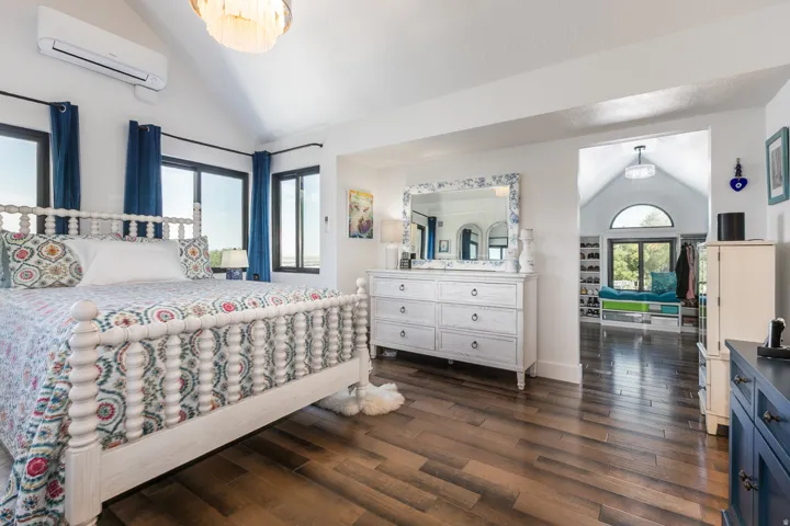 Vaulted ceiling room featuring wood-finish flooring, multiple windows, a decorative chandelier, and a wall-mounted air conditioning unit