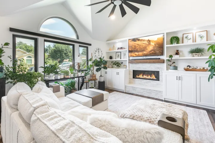 Vaulted ceiling living area featuring a semi-circular window, black-framed windows, built-in shelving, a linear fireplace with a stone surround, and wood-finish flooring