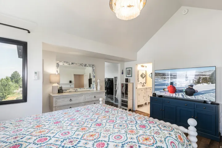 Vaulted ceilings with a decorative chandelier, a large picture window, and wood-finish flooring