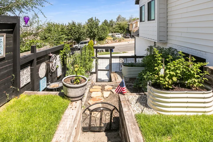 Tiered yard space featuring a black privacy fence with decorative accents, a stone pathway, and multiple raised garden beds