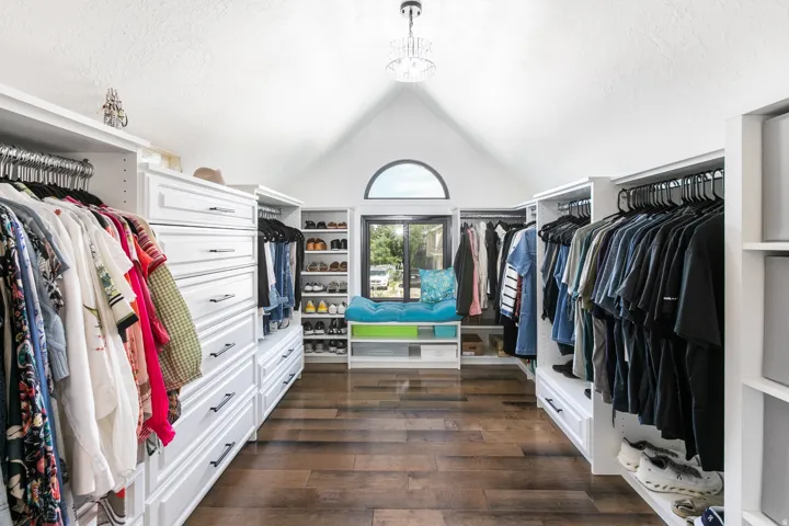 Spacious closet featuring abundant built-in cabinetry, wood-finish flooring, a vaulted ceiling, and an arched window