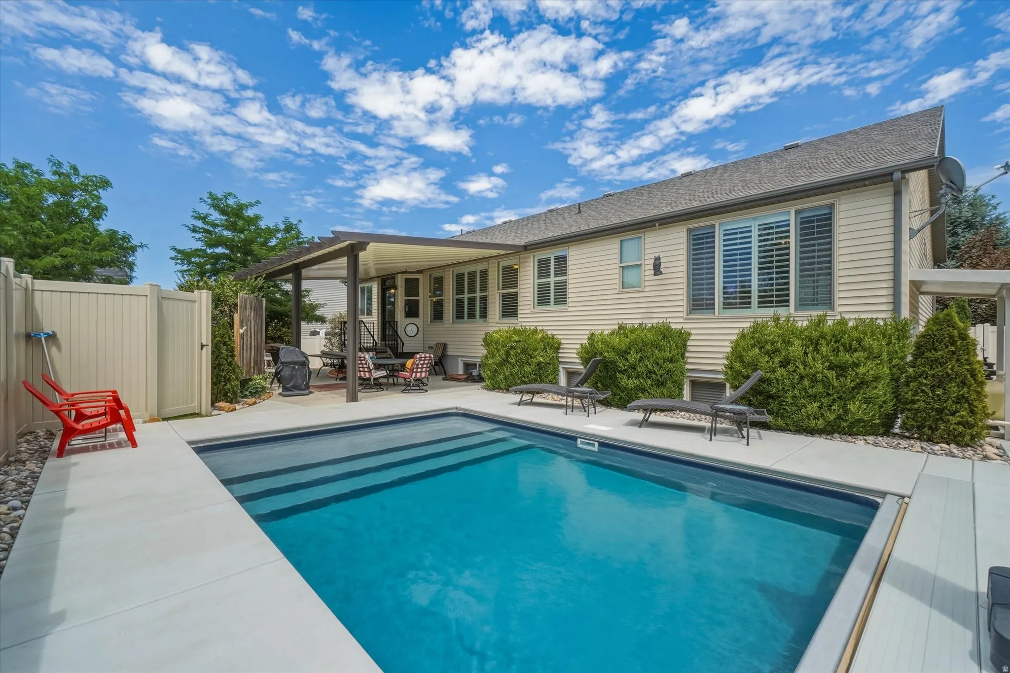 Outdoor pool with concrete decking, a covered patio, and privacy fencing