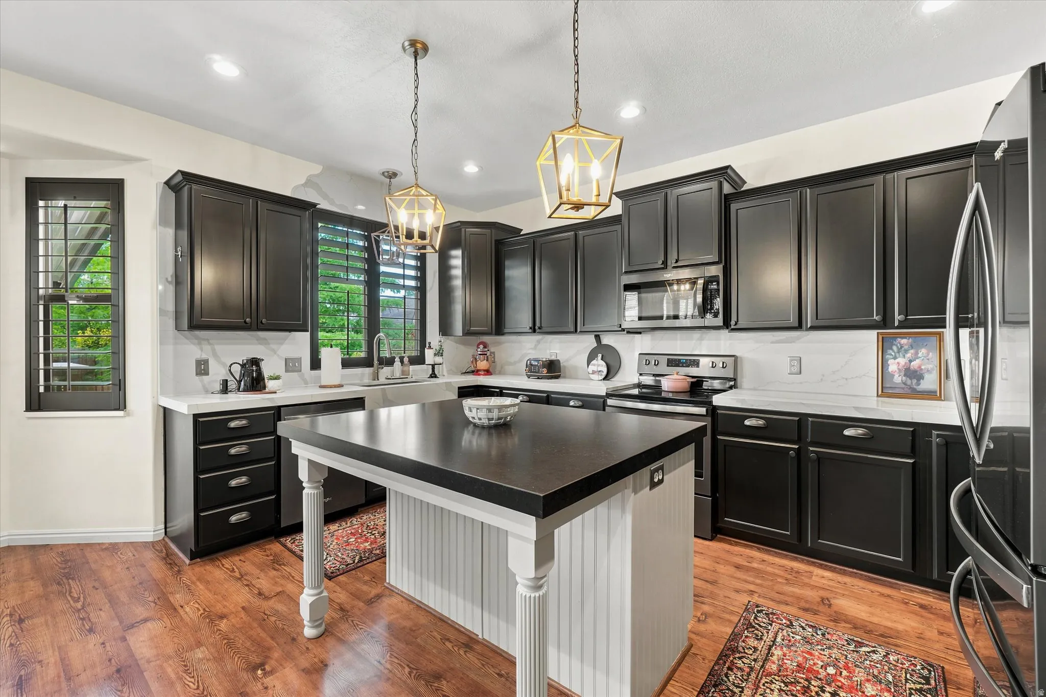 Gourmet kitchen featuring dark cabinetry, white countertops, a large island with beadboard paneling, stainless steel appliances, and two brass pendant lights