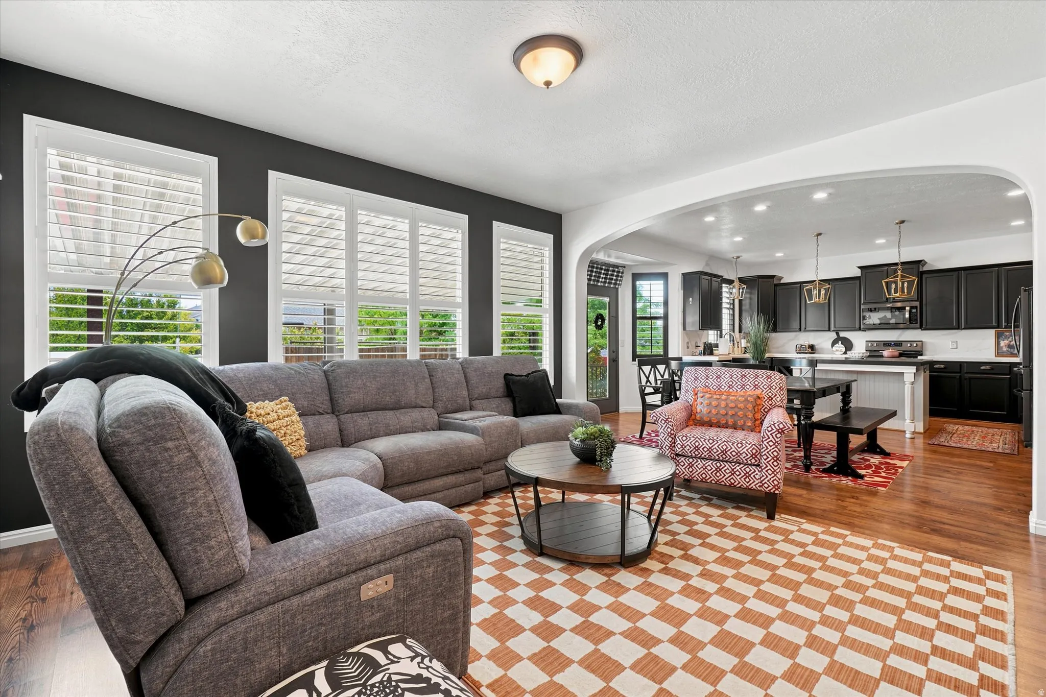 Living area with dark accent wall, featuring multiple windows with white plantation shutters and wood-finish flooring