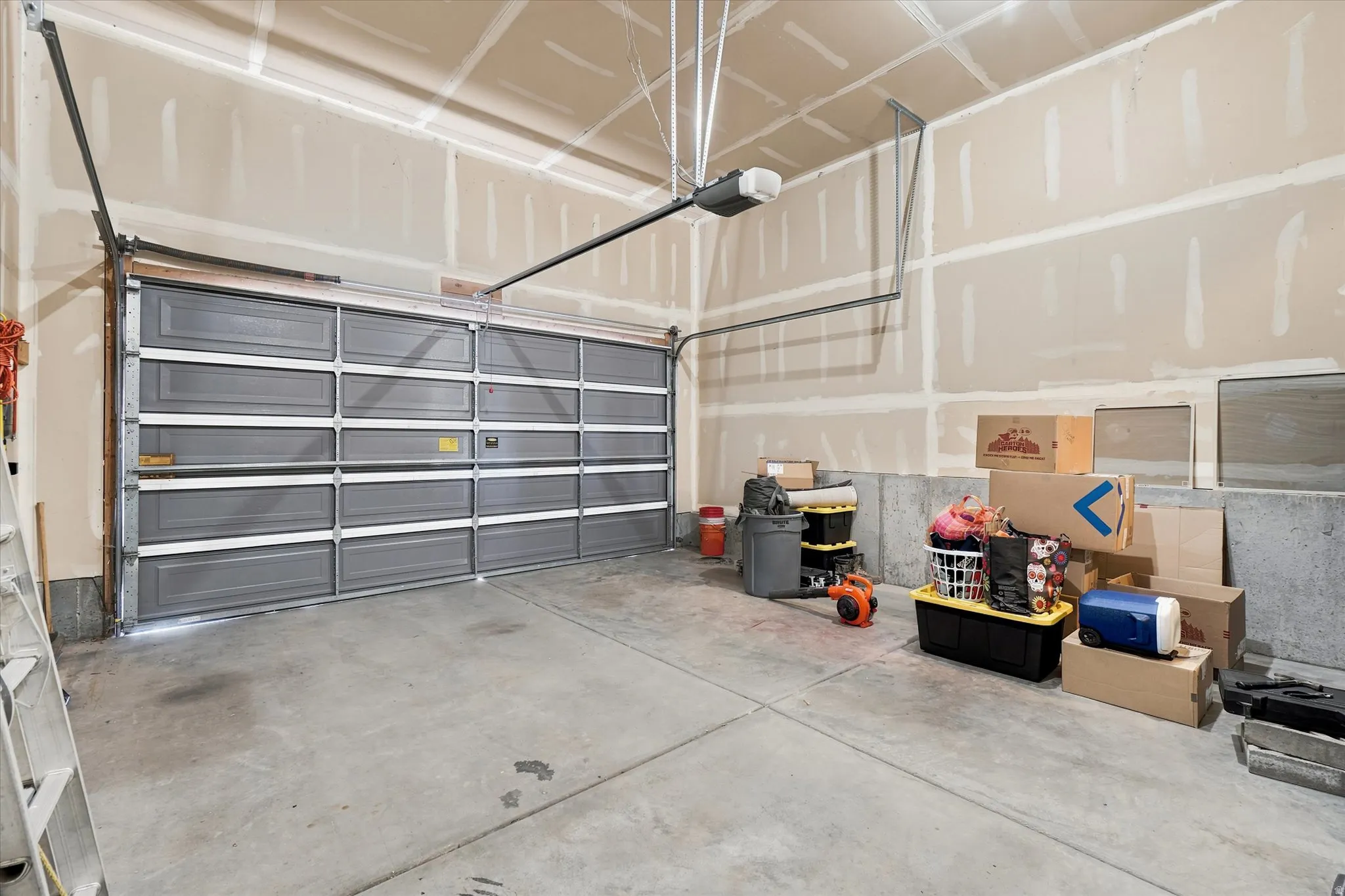 Spacious garage featuring a grey paneled door with white accents, concrete flooring, and a ceiling-mounted garage door opener
