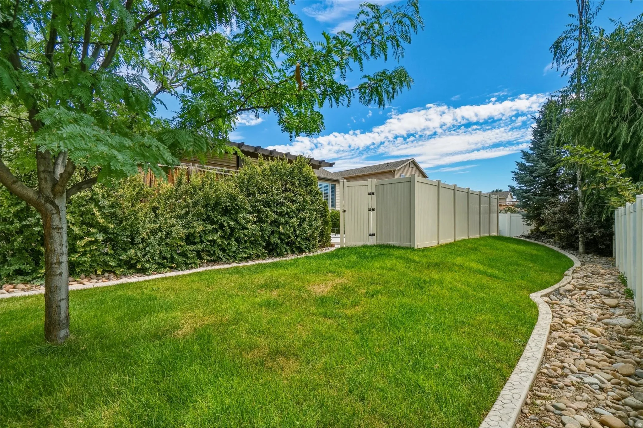 Expansive backyard featuring a lush lawn, mature trees, and a stone-lined dry creek bed