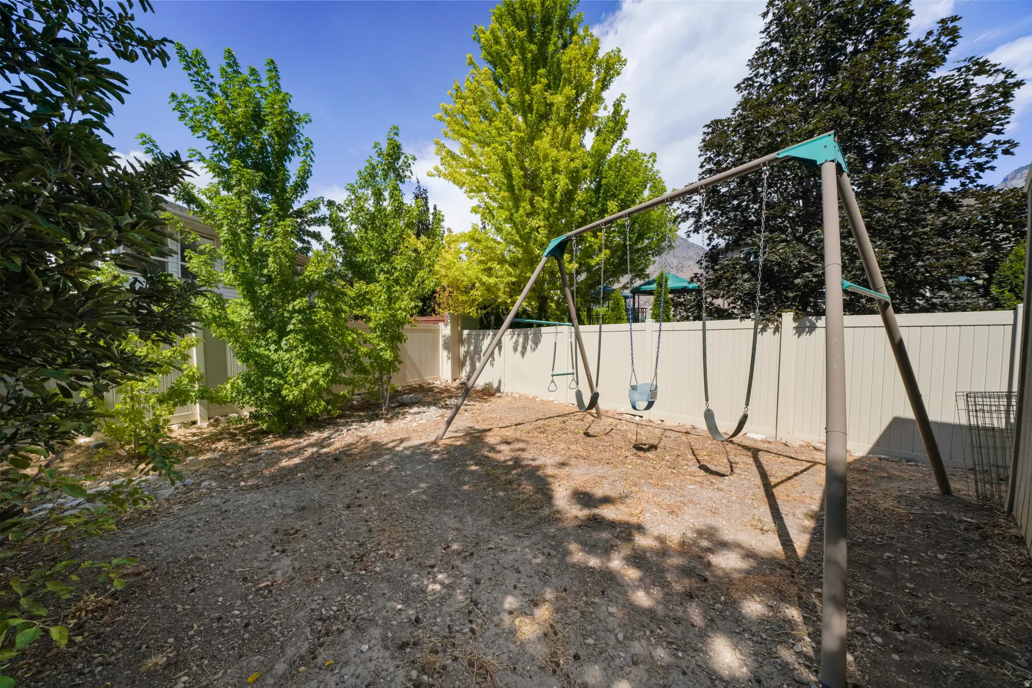 Fenced backyard area featuring a swing set, mature trees, and a gravel ground cover