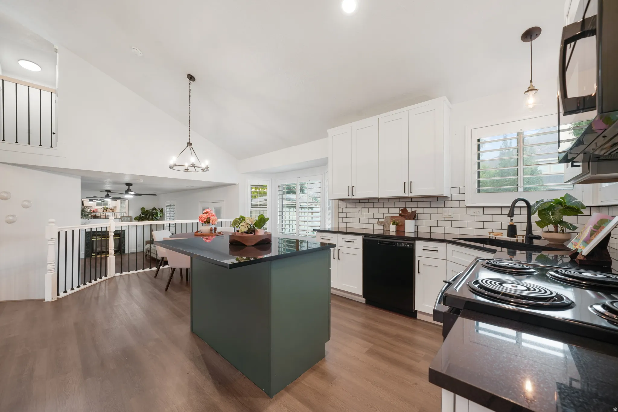 Spacious kitchen featuring an island with countertop seating, white shaker cabinetry, black appliances, white subway tile backsplash, and light wood-finish flooring