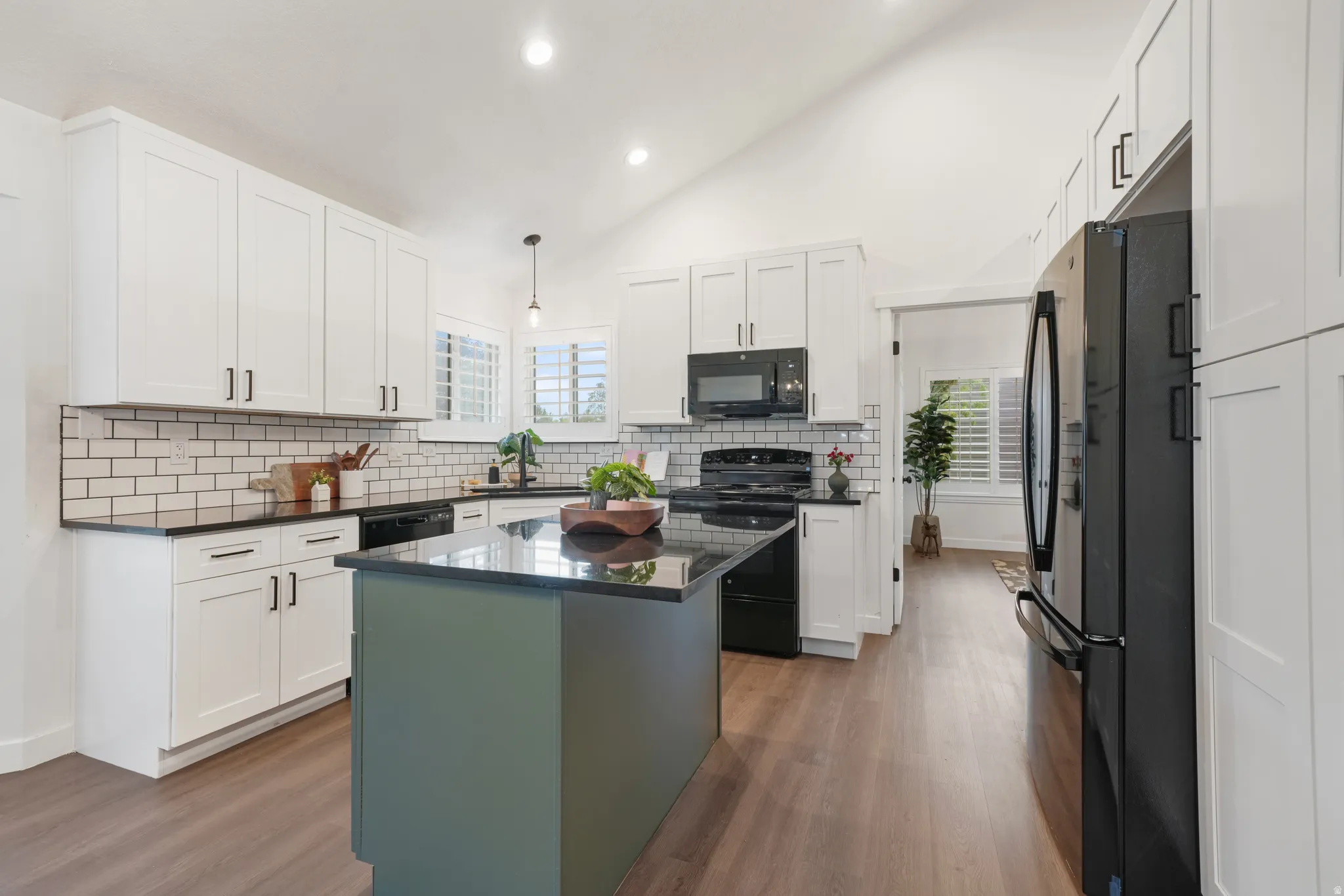 Modern kitchen featuring a central island with a dark countertop, white shaker-style cabinetry, subway tile backsplash, and dark wood-finish flooring