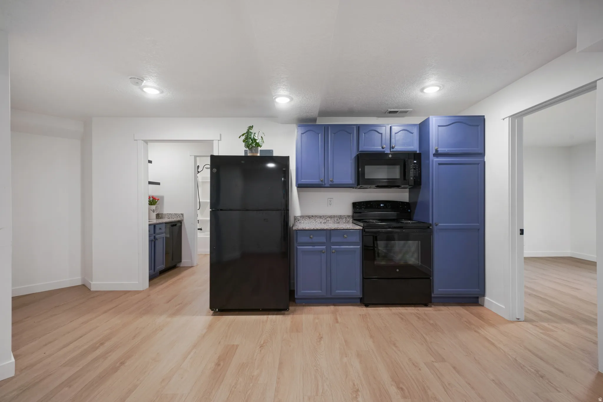 Kitchen featuring wood-finish flooring, blue cabinetry, black appliances, and granite-style countertops