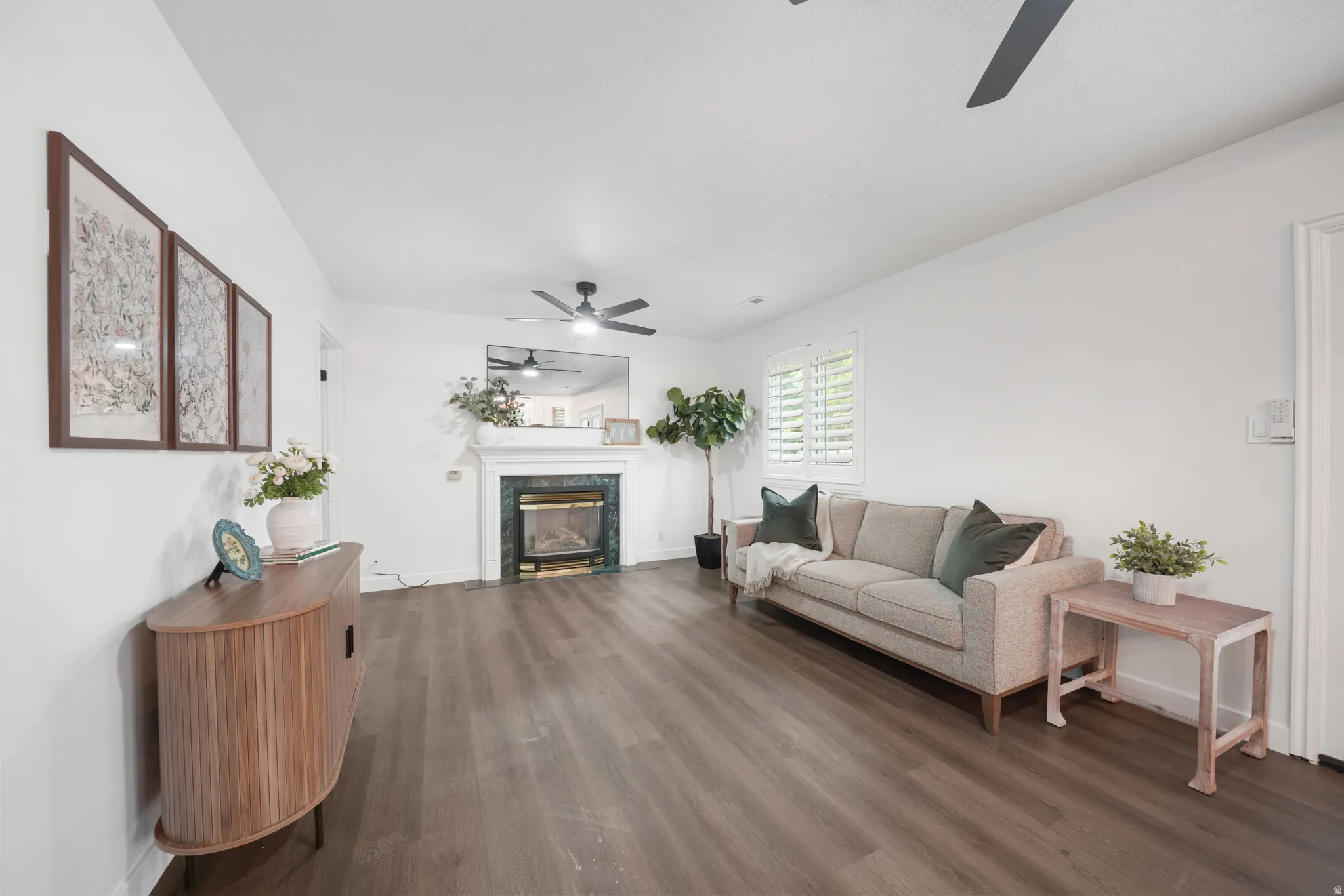 Living area featuring wood-finish flooring, a fireplace with a white mantel and dark stone surround, and ceiling fans