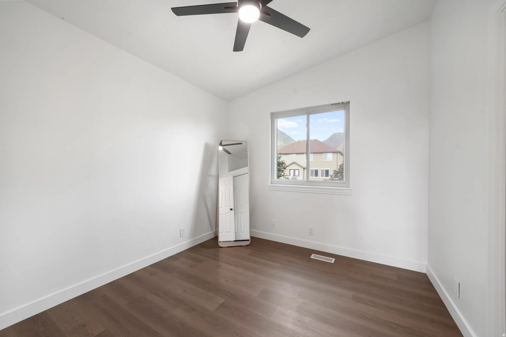 Spacious room featuring wood-finish flooring, crisp white walls, and a contemporary ceiling fan