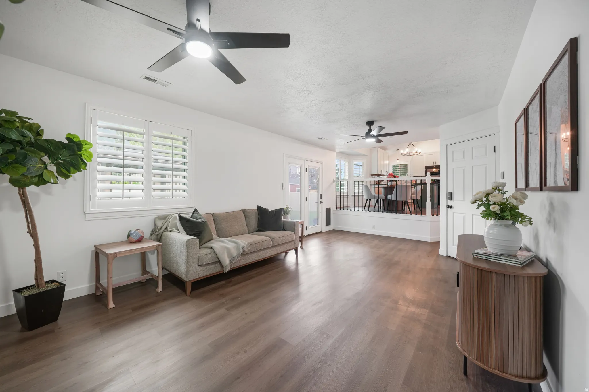 Spacious living area featuring wood-finish flooring, white walls, and a recessed ceiling with modern black ceiling fans