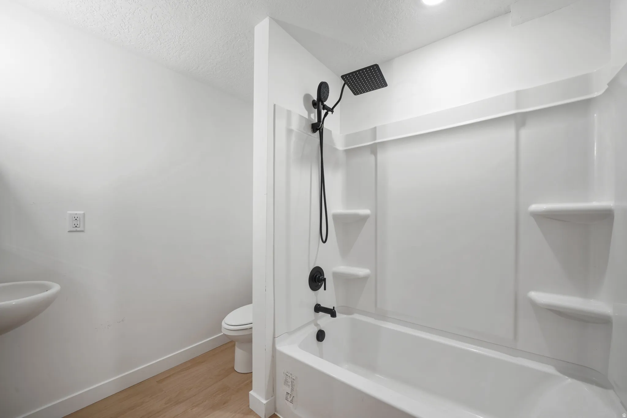 Bathroom featuring a white tub-shower combination with matte black fixtures, rain shower head, and built-in shelving