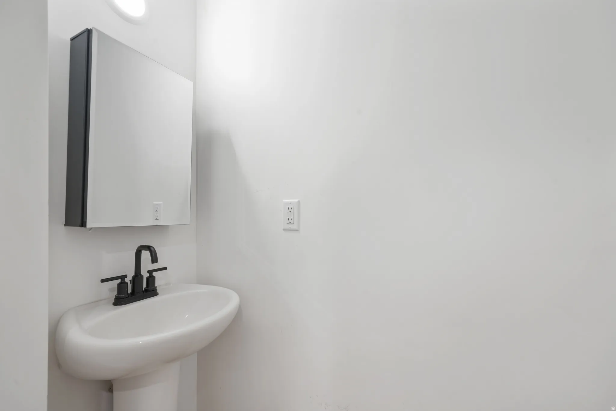 White pedestal sink with a matte black faucet, complemented by a medicine cabinet with a mirrored door