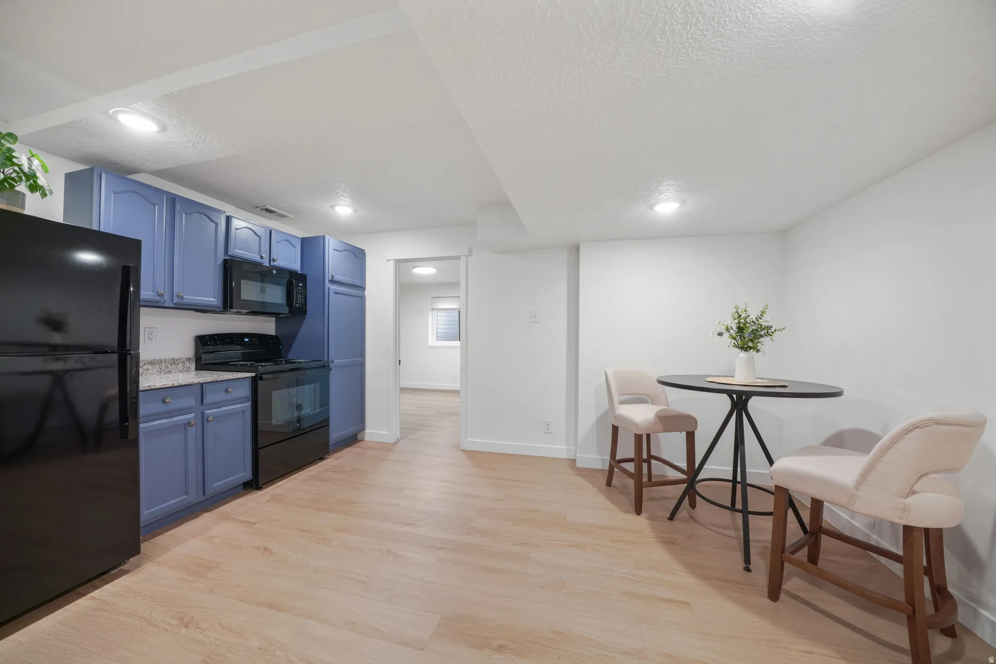 Kitchen area featuring light wood-finish flooring, blue cabinetry, stone-finish countertops, and recessed lighting