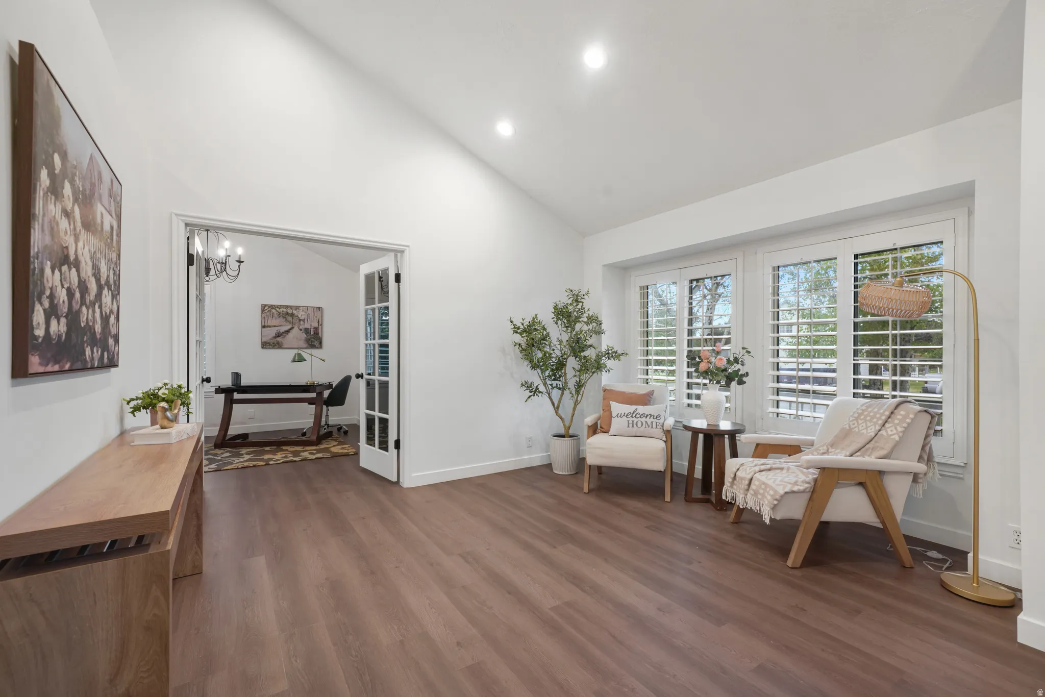 Living area featuring wood-finish flooring, vaulted ceilings, recessed lighting, and a bay window with plantation shutters