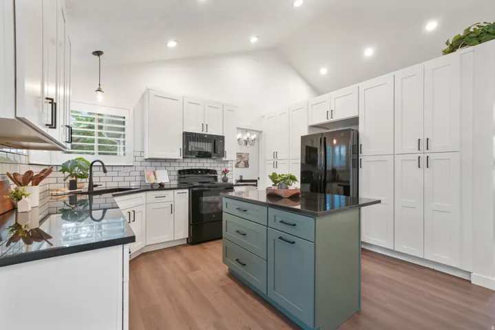 Kitchen featuring a vaulted ceiling with recessed lighting, dark countertops, white shaker cabinetry with black hardware, and a contrasting island with storage