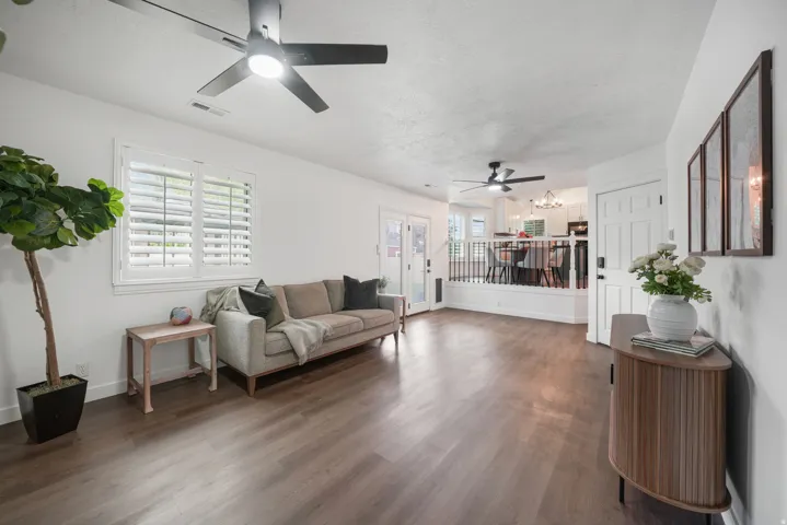 Spacious living area featuring wood-finish flooring, white walls, and a recessed ceiling with modern black ceiling fans