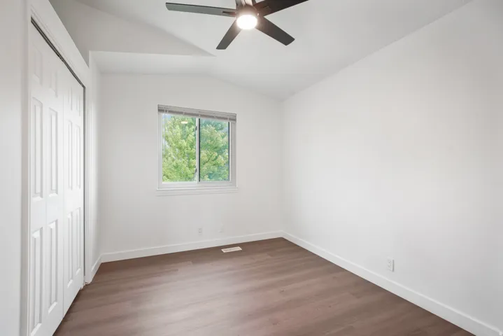Room featuring vaulted ceilings, wood-finish flooring, a ceiling fan, and a window with roller blinds