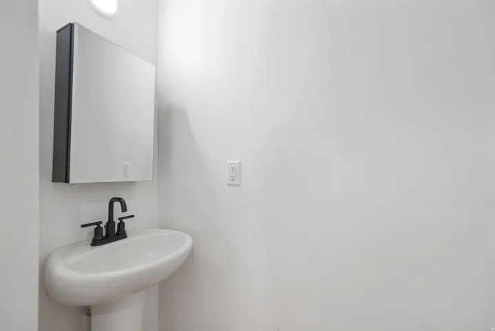 White pedestal sink with a matte black faucet, complemented by a medicine cabinet with a mirrored door