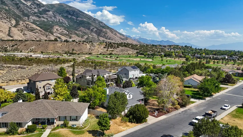 Mountain backdrop with a golf course, residential properties, clear blue sky, and a paved street