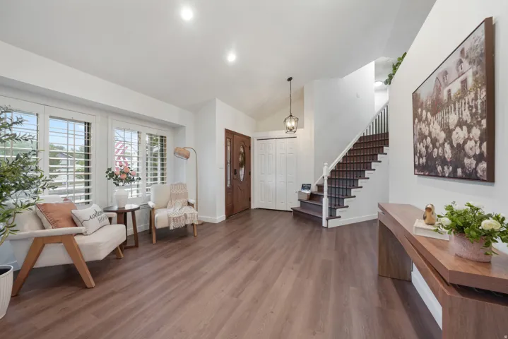Spacious entry area featuring rich wood-finish flooring, a grand staircase with dark wood treads and white risers, and a prominent front door