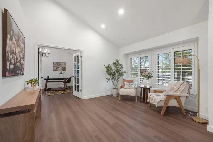 Living area featuring wood-finish flooring, vaulted ceilings, recessed lighting, and a bay window with plantation shutters