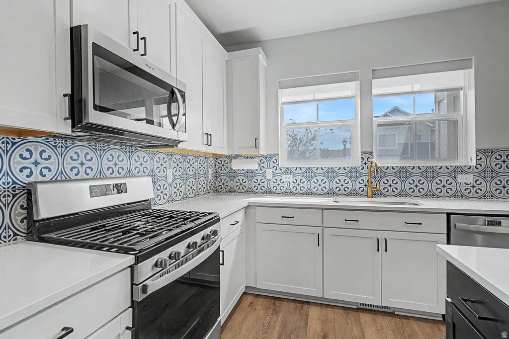 Kitchen featuring white cabinetry, patterned tile backsplash, stainless steel appliances, white countertops, and wood-finish flooring