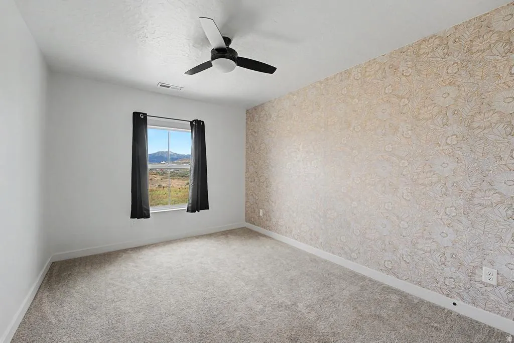 Room featuring a patterned accent wall, white painted walls, and light-colored carpet flooring
